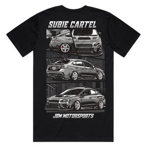 May include: A black t-shirt featuring a graphic print with the text SUBIE CARTEL at the top and JBM MOTORSPORTS at the bottom. The design displays three grayscale illustrations of a sedan car from different angles, including front and rear views.