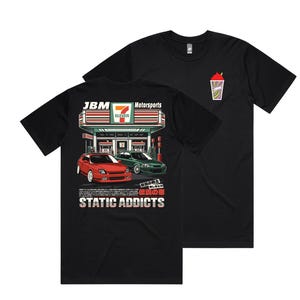 May include: Black t-shirt featuring a graphic of two red and green cars parked in front of a 7-Eleven store. The text "JBM Motorsports" and "STATIC ADDICTS" is printed on the shirt.