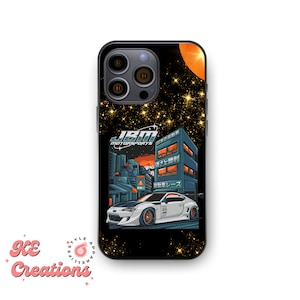 May include: Black phone case with a white car and city skyline design. The car has the text "JBM MOTORSPORTS" on the side. The city skyline has Japanese text on the buildings. The background is a black and gold starry night.