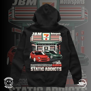 May include: Black hoodie with a graphic of a 7-Eleven convenience store with two cars parked in front. The text "JBM Motorsports" and "STATIC ADDICTS" is printed on the hoodie.