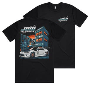 Puede incluir: Camiseta negra con un coche blanco y texto japonés en la parte delantera. El texto dice "JBM Motorsports".