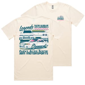 May include: Cream-colored t-shirt featuring a graphic of three white sports cars with pink and blue accents. The shirt has the text "Legends", "Racing Bloodline GTR Supremacy", and "Japan Auto Scene JBM Motorsports". A smaller graphic is on the upper right.