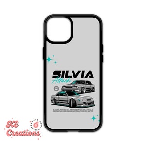 May include: A gray iPhone case with a black border. The case features a graphic of two silver Nissan Silvias with the text "SILVIA Attack" in blue and white. The background is a light gray with silver stars.