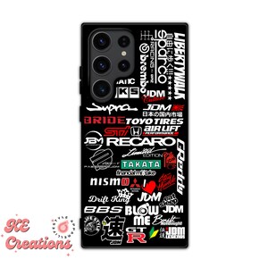 May include: Black phone case with a collage of Japanese car and racing logos, including "Supra", "JDM", "Recaro", "Bride", "Takata", "Nismo", "BBS", "Drift King", "Blow Me", "GT-R", and "Liberty Walk".
