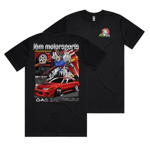 May include: Black t-shirt featuring a graphic design with a red sports car and a robot. The text "jbm motorsports" is displayed above the car and robot. A smaller logo is on the upper right chest.