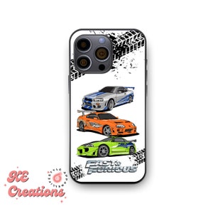 May include: White iPhone case with a black and white tire tread pattern. The case features three cartoon cars from the Fast and Furious franchise: a white Nissan Skyline GT-R, an orange Toyota Supra, and a green Mitsubishi Eclipse. The text "Fast & Furious" is printed on the case.