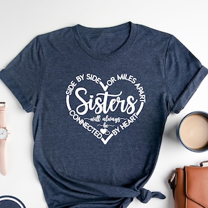 May include: A navy blue t-shirt with a white heart graphic that says "Side by side or miles apart, Sisters will always be connected by heart".