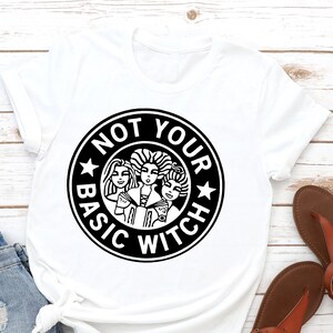 May include: White t-shirt with a black circle graphic that says "Not Your Basic Witch" with three witches inside the circle.