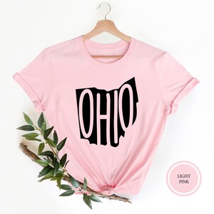 May include: A light pink t-shirt with a black outline of the state of Ohio and the word "OHIO" written inside the outline.