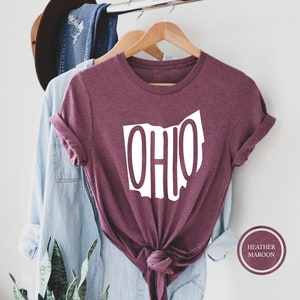 May include: A heather maroon t-shirt with a white outline of the state of Ohio and the word "OHIO" written inside the outline. The shirt is tied in a knot at the bottom.