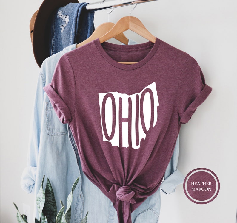 May include: A heather maroon t-shirt with a white outline of the state of Ohio and the word "OHIO" written inside the outline. The shirt is tied in a knot at the bottom.