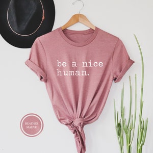 Pu&ograve; includere: Una t-shirt color malva con la scritta "be a nice human." stampata in bianco.