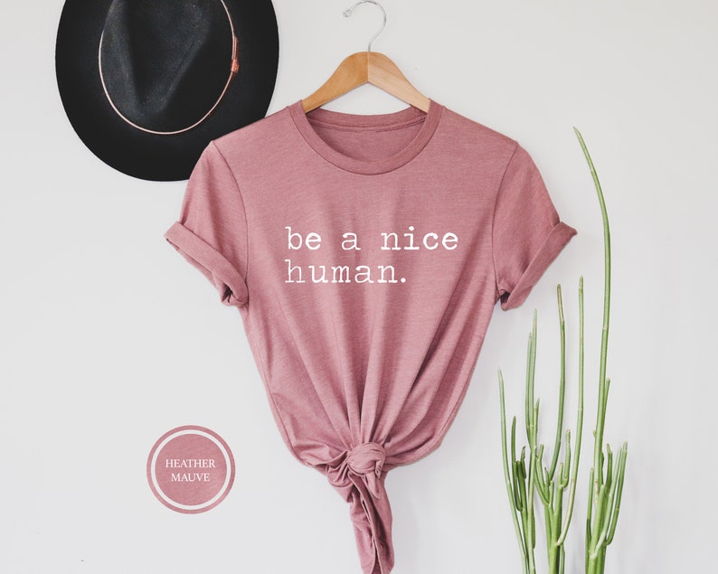 Pu&ograve; includere: Una t-shirt color malva con la scritta "be a nice human." stampata in bianco.