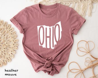 May include: A heather mauve short-sleeve t-shirt featuring a white graphic of the state of Ohio with the word OHIO printed in a bold, sans-serif font that fills the shape of the state outline. The shirt has a crew neckline and rolled sleeves.