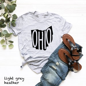 May include: A light grey heather t-shirt with a black graphic of the state of Ohio with the word "OHIO" inside the outline of the state.