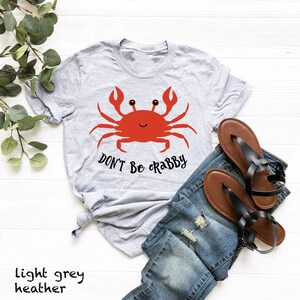 May include: Light grey heather t-shirt with a red cartoon crab and the text "Don't Be Crabby".