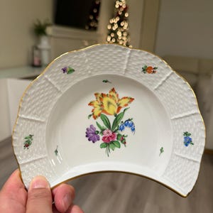 May include: White porcelain serving dish with a floral design. The dish has a scalloped edge with a gold trim. The center of the dish features a bouquet of colorful flowers, including yellow, purple, and blue blooms.