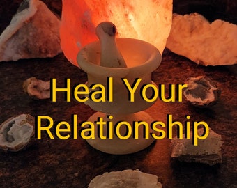 May include: A white mortar and pestle sits on a wooden surface with a Himalayan salt lamp glowing behind it. The text "Heal Your Relationship" is written in yellow on the surface. There are several crystals scattered around the mortar and pestle.