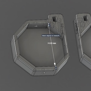 May include: Two gray, hexagonal, 3D-modeled containers with a small tab featuring a hole at the top. A digital measurement tool indicates an internal width of 74.00 mm across the flat sides of the left container, which is displayed on screen.
