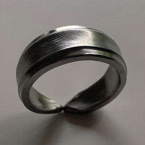 May include: A silver ring with a textured, grooved design. The ring is open on one side, making it adjustable.