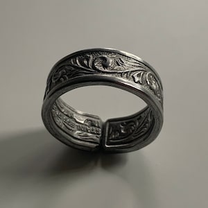 Puede incluir: Un anillo de plata con un diseño floral. El anillo está abierto y tiene un cierre con bisagra.