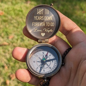 May include: A brass compass with a lid that reads "YEARS DOWN, FOREVER TO GO Love, Kayla". The compass has a green jewel in the center and a black needle.