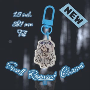 May include: A small, clear Revenant charm with a blue clasp. The charm features a cartoon illustration of a figure with long white hair, a floral crown, and a harp. The charm is 1.5 inches (38.1 mm) tall. The word "NEW" is in a blue box.