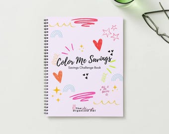 Op de afbeelding: Een spiraalgebonden notitieboek met een lichtroze kaft met de tekst "Color Me Savings" en kleurrijke krabbels. Het notitieboek bevat harten, sterren en regenbogen. De woorden "Savings Challenge Book" zijn ook zichtbaar.