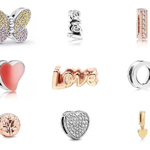 May include: A collection of silver and gold-toned charms. Charms include a butterfly with yellow and pink stones, the word "love", a heart, a tree, and a gold heart pendant. These charms are likely for a bracelet or necklace.