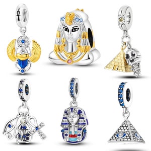 May include: Six silver charm pendants with Egyptian themes. The charms feature a pharaoh, an ankh, an eye of Horus, a pyramid, and a scarab beetle. The charms are decorated with blue and gold accents.