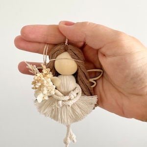 May include: A small wooden doll with brown yarn hair, white yarn wings, and a white yarn dress. The doll is holding a bouquet of dried white flowers.