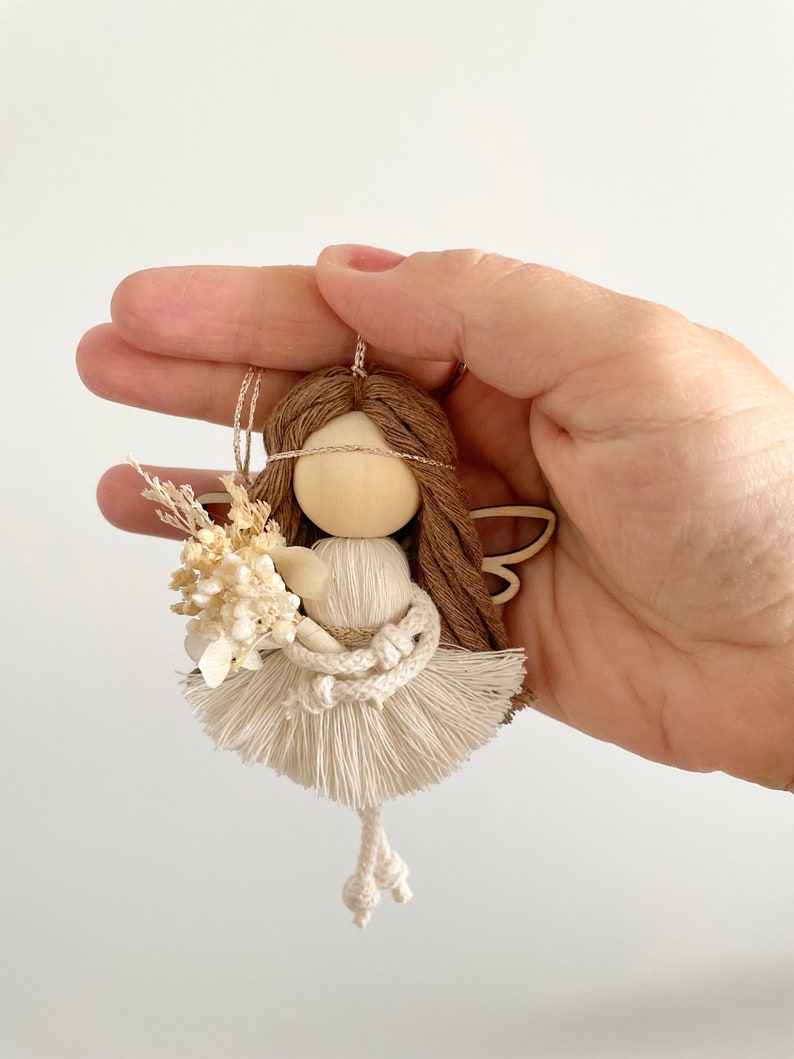 May include: A small wooden doll with brown yarn hair, white yarn wings, and a white yarn dress. The doll is holding a bouquet of dried white flowers.