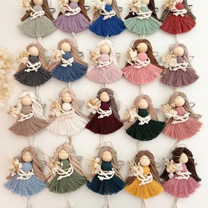 Può includere: Ventiquattro ornamenti di angelo in filato fatti a mano in vari colori, tra cui beige, marrone, blu, verde, rosa, rosso e bianco. Ogni angelo ha una testa di legno, capelli di filato e un vestito di filato bianco con un piccolo bouquet di fiori secchi.
