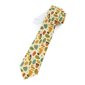 May include: A necktie with a retro mid-century modern design. The tie features a cream-colored background with a repeating pattern of abstract shapes in orange, green, yellow, and black. The tie's knot is white.