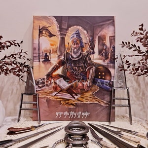 May include: An artistic canvas print depicting a historical figure in traditional attire, seated and reading. The image is flanked by decorative metal objects, including knives and rings, arranged on a textured surface. The print features text in a foreign language.
