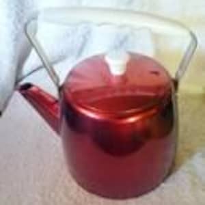 May include: A red metallic tea kettle with a white handle and lid. The kettle has a spout and a curved handle that arches over the top. The kettle is sitting on a white surface.