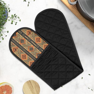 May include: A pair of black oven mitts with a quilted design. One mitt has a brown and orange geometric pattern.