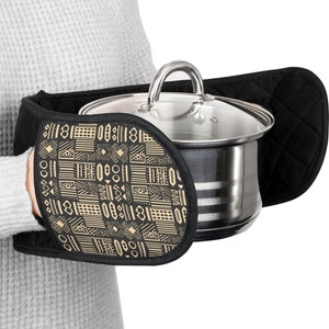 May include: Black and gold patterned oven mitt with a quilted design. The mitt is holding a stainless steel pot with a glass lid.