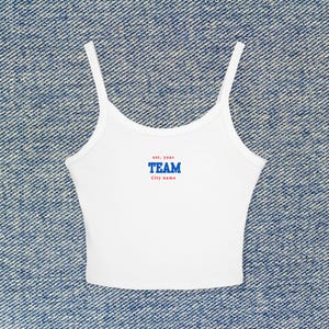 May include: White crop top with thin straps. The top features the text "est. year" in red, above the word "TEAM" in blue, and "City name" in red. The top is made of a soft, lightweight material.