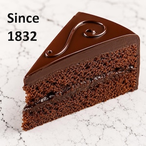Puede incluir: Una porción triangular de pastel de chocolate oscuro con dos capas de bizcocho y relleno de chocolate, cubierta con una ganache de chocolate suave con un remolino decorativo. El texto "Since 1832" es visible en la esquina superior izquierda.