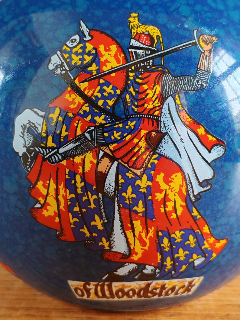 May include: A blue decorative object featuring a knight on horseback, rendered in red, yellow, and blue heraldic designs. The knight is holding a sword, and the object has the text "of Woodstock" at the bottom.