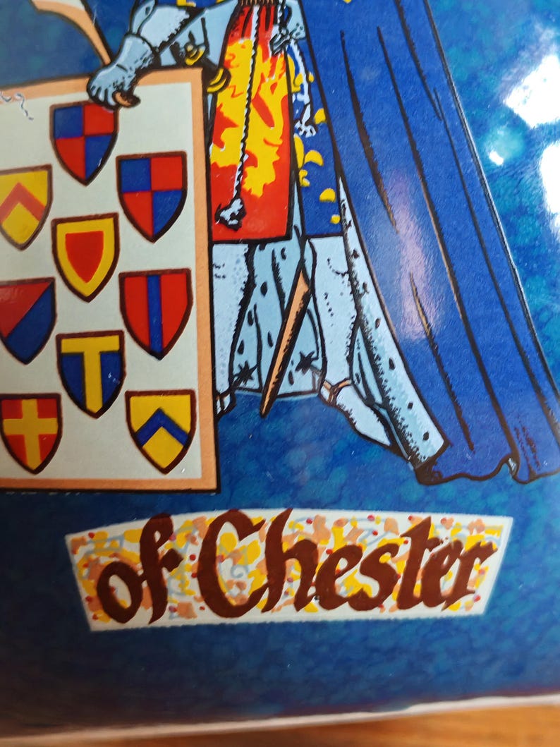 May include: A blue and white illustration featuring a knight holding a shield with various heraldic emblems. The text "of Chester" is displayed in a decorative banner. The artwork has a vintage, possibly antique, aesthetic.