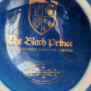 May include: Close-up of a blue porcelain object with gold lettering and a gold emblem. The text reads "The Black Prince Scotch Whisky Company Limited" and "Genuine British Porcelain".