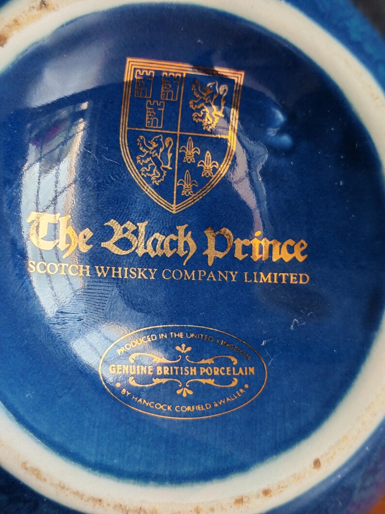 May include: Close-up of a blue porcelain object with gold lettering and a gold emblem. The text reads "The Black Prince Scotch Whisky Company Limited" and "Genuine British Porcelain".