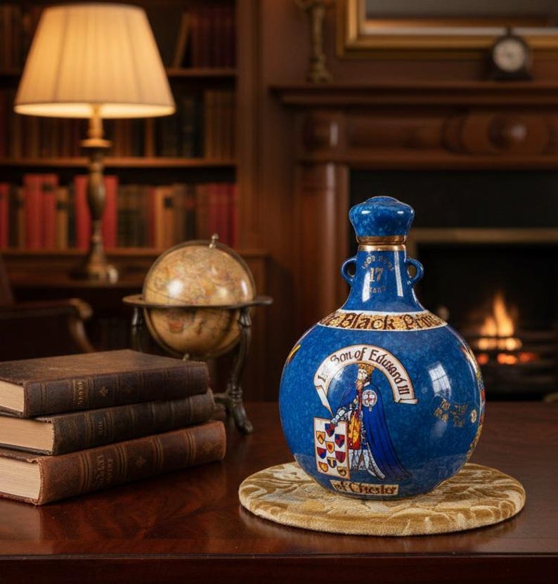 May include: A blue ceramic decanter with a detailed illustration of a historical figure and text. The decanter has a matching stopper and gold accents. The text reads "Son of Edward III" and "Black Prince".