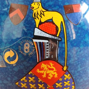 May include: A blue ceramic decorative object with a yellow lion and crown design. The object features a red and gold emblem, along with the text "COTISATION SECURITE SOCIALE".