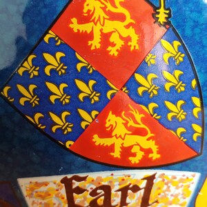 May include: Close-up of a shield design with a blue background. The shield is divided into sections of red with a yellow lion and blue with yellow fleur-de-lis. The word "Earl" is written in brown script.