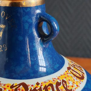 May include: Close-up of a blue ceramic bottle with gold accents. The bottle has a handle and a decorative band with text. The bottle's surface has a speckled pattern. The text on the bottle reads "OVER 17 YEARS" and "Prince".