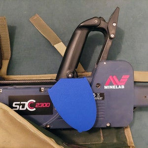 May include: A blue and black metal detector with a blue protective cover and the text "SDC 2300" and "MINELAB" on the side.