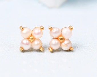 May include: A pair of gold stud earrings with four small white pearls arranged in a square shape.